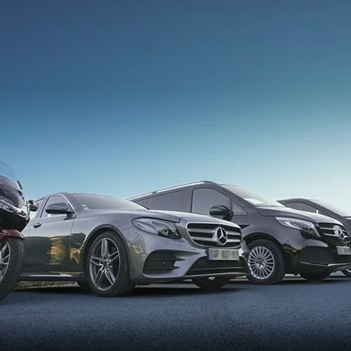 Berline Mercedes grise et vans noirs alignés sur un parking.