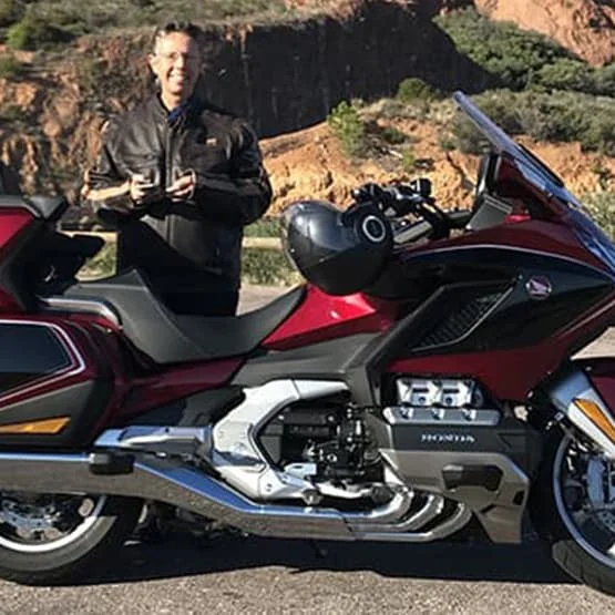 Homme en costume près d’une moto de tourisme rouge.